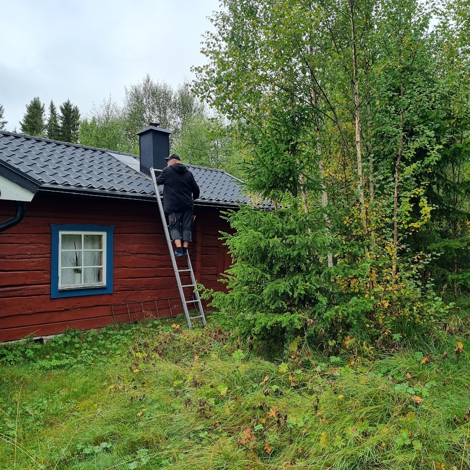 Plåtslagare på stege vid röd stuga, takarbete